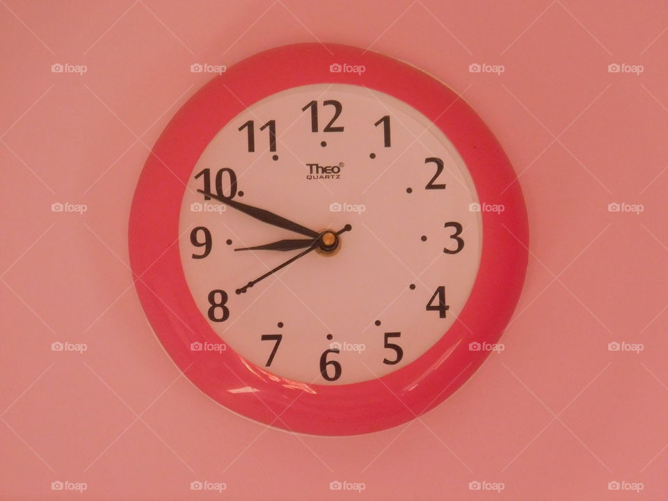Analog watch or clock hanging on wall. It is white dialed ellipse shaped clock.