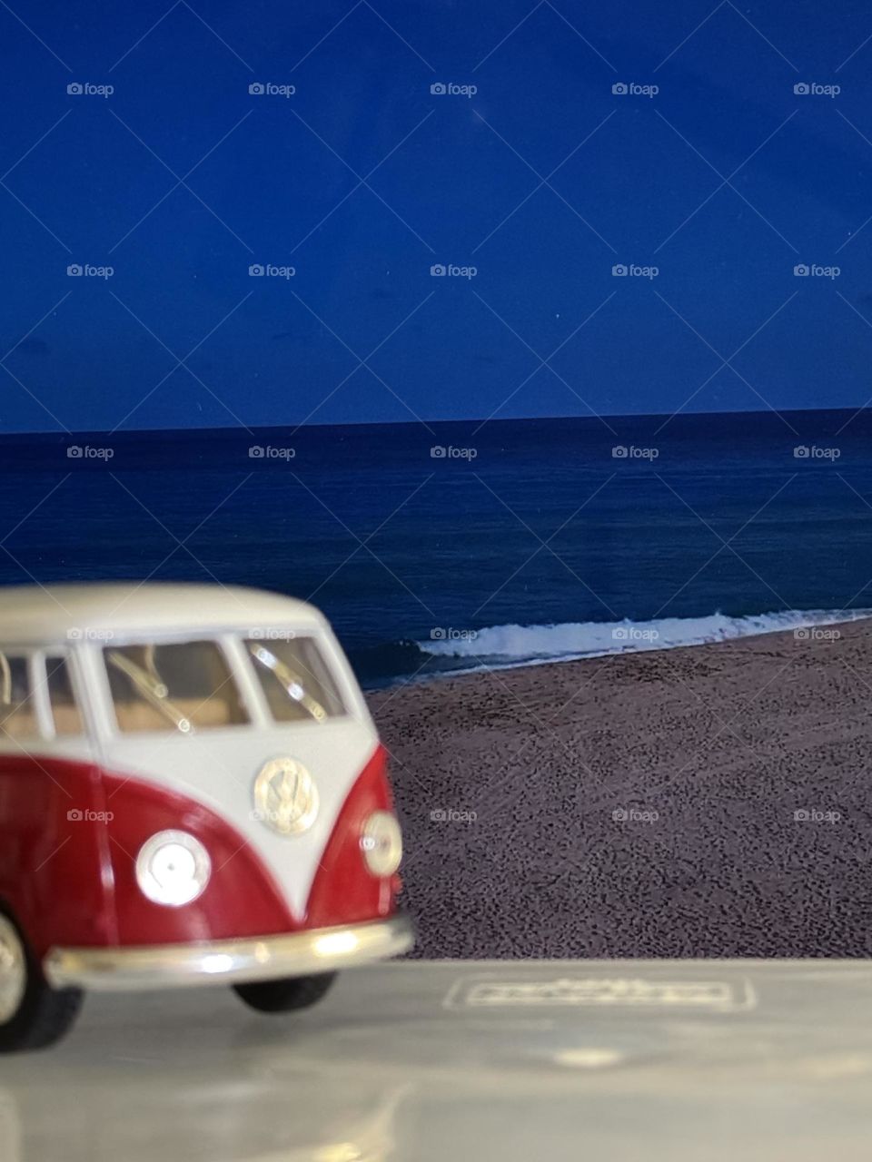 Toy VW bus on clear plastic surface in front of computer screenshot of Hawaii’s famous Pipeline flat in off season 