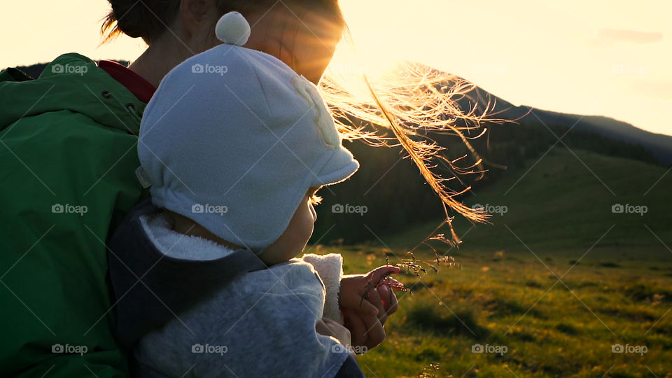 Foreground is the baby.  Intense sunlight passes through the mother's hair. Mother'S face is hidden. Setting down sun. Concept of love and family