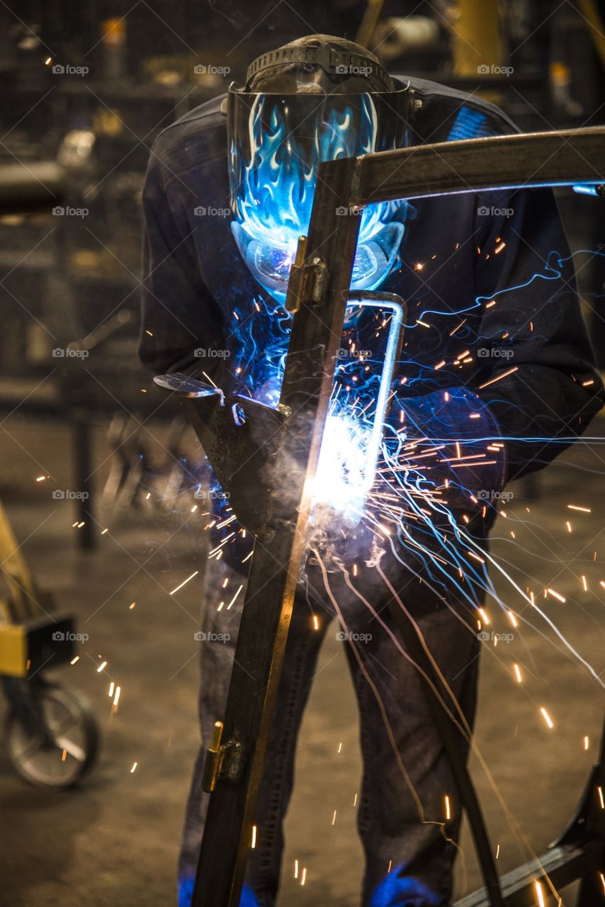 This welder is building a frame by welding bar steel together using fixtures to produce a ROPS frame for a heavy equipment Cab. 