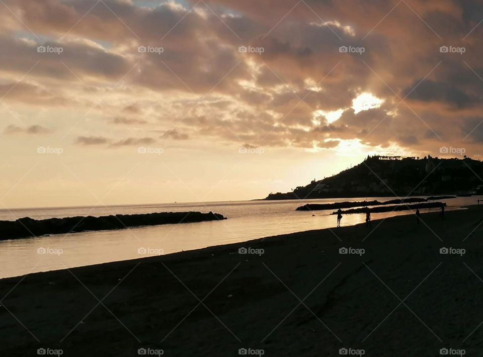 Evening.  The sun has set behind the mountains.  Sea shore.  Small clouds in the sky