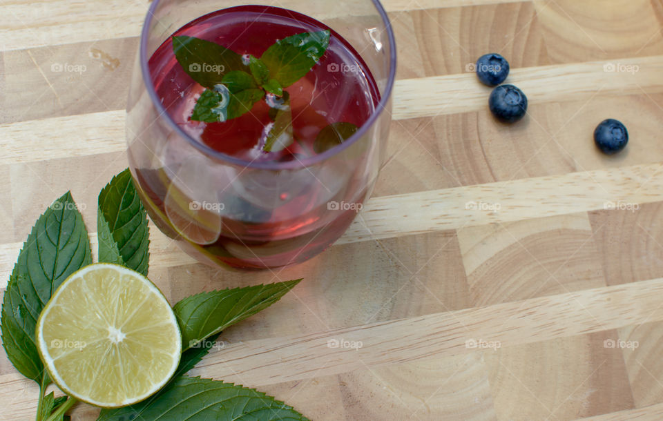 High angle view of beautiful homemade blueberry, lime and mint flavored water or juice with fresh ingredients on wood table with sliced cross section of lime