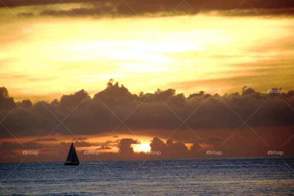 A sailboat sailing at sunset with a distant storm upon the ocean