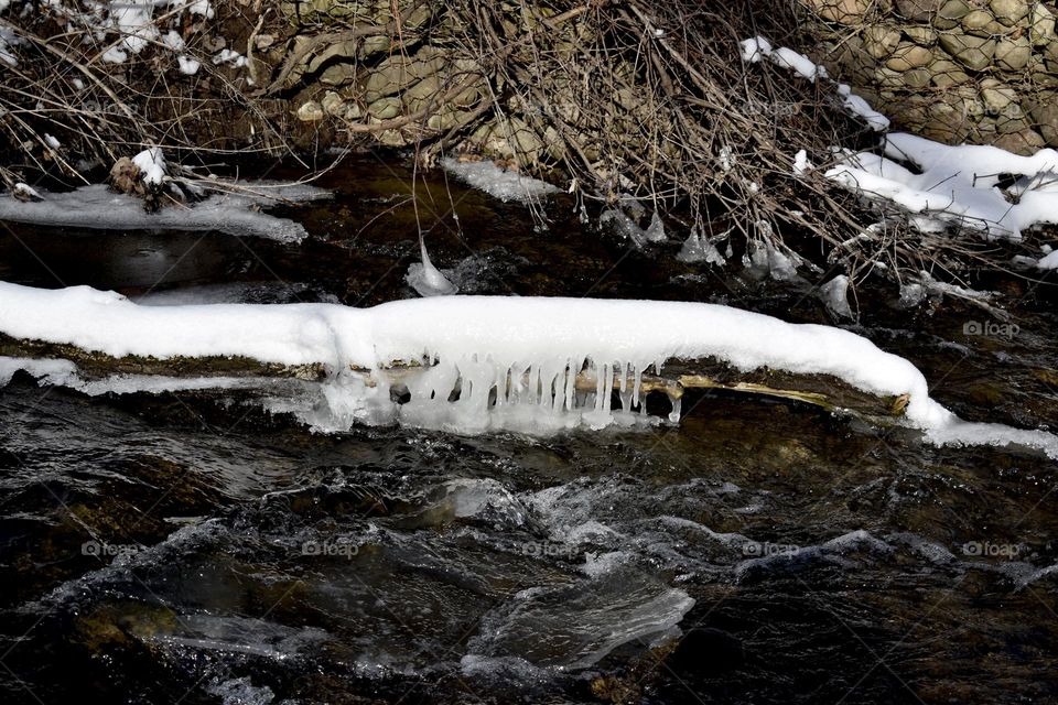 A snow and ice covered log in the cold stream