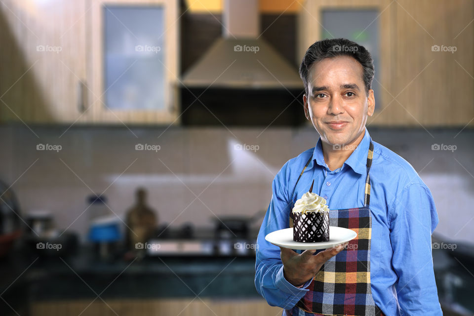Indian chef in kitchen interiors with a chocolate cake