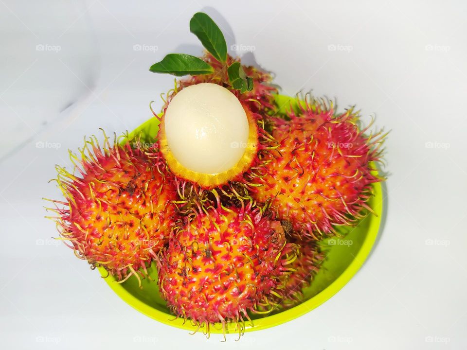 Some rambutan fruit in green bowl isolated on white background