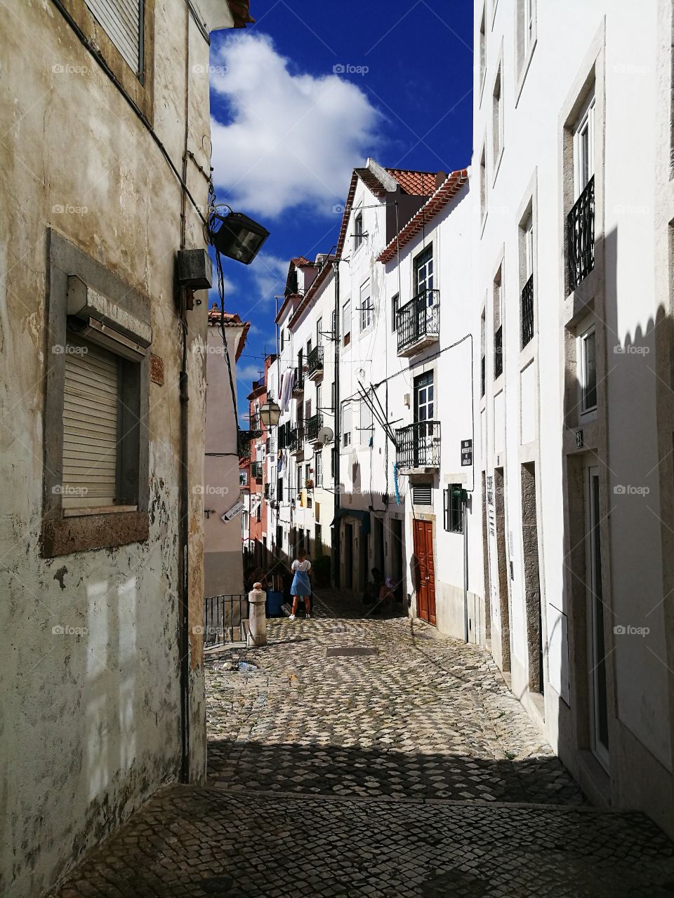 Bright sunlight enhances the white walls of the buildings of the narrow streets of Alfama, Lisbon.