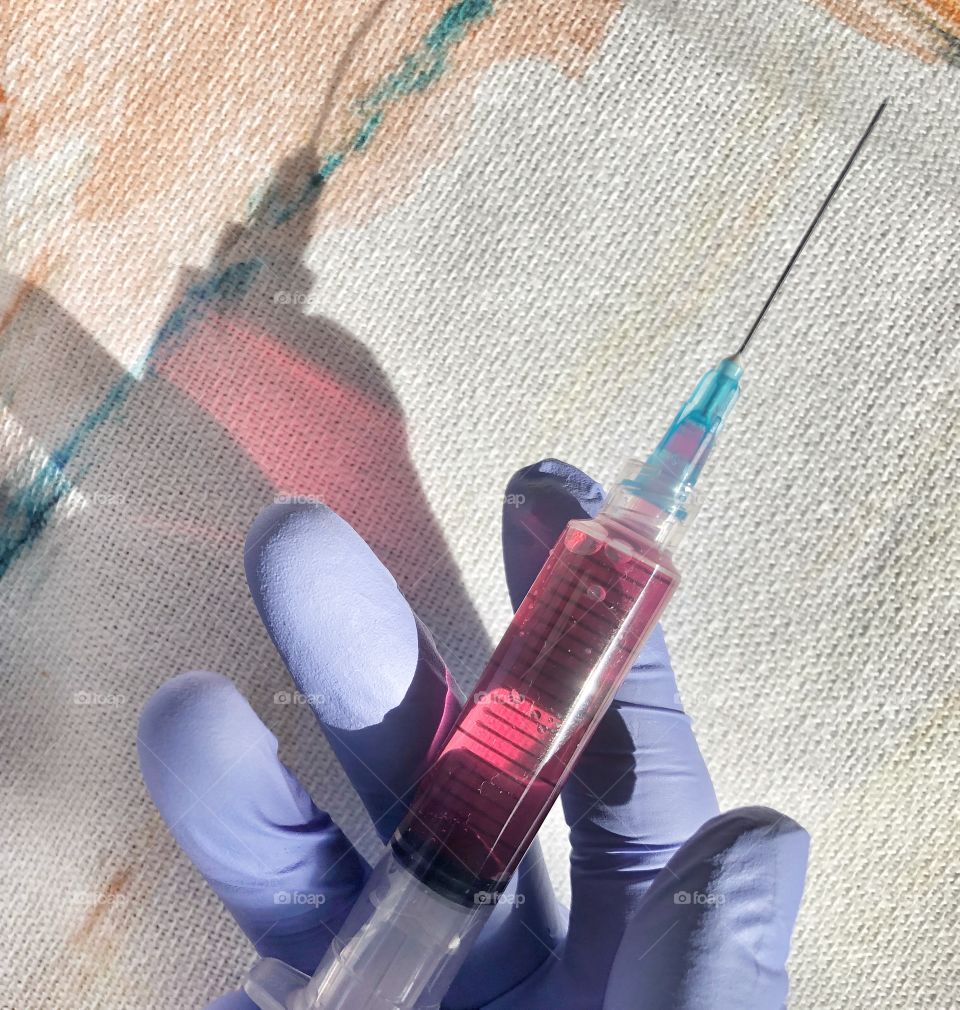 Purple latex gloved hands holding pink Medicine filled syringe to inject