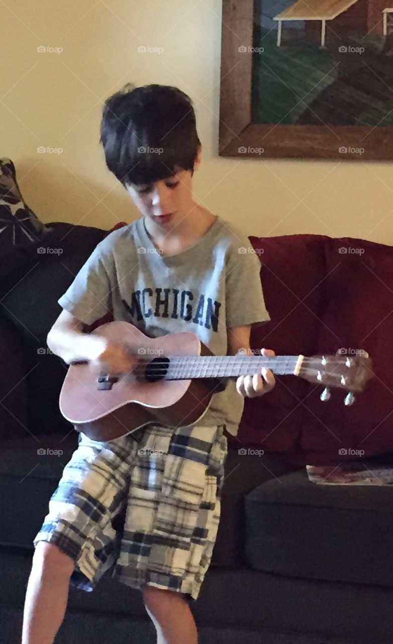 Young boy sitting on the couch, playing the ukelele instrument.