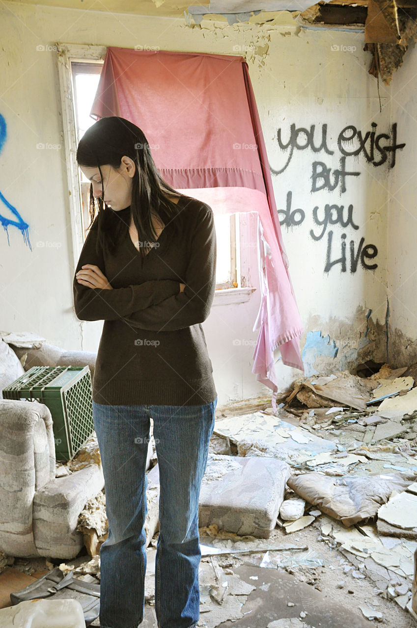 a young woman is seen in an abandon house with litter and graffiti. You exist, but do you live.