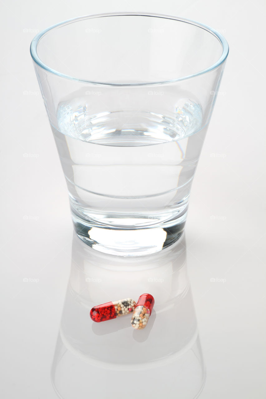 Medicine Capsules and glass on white reflective background