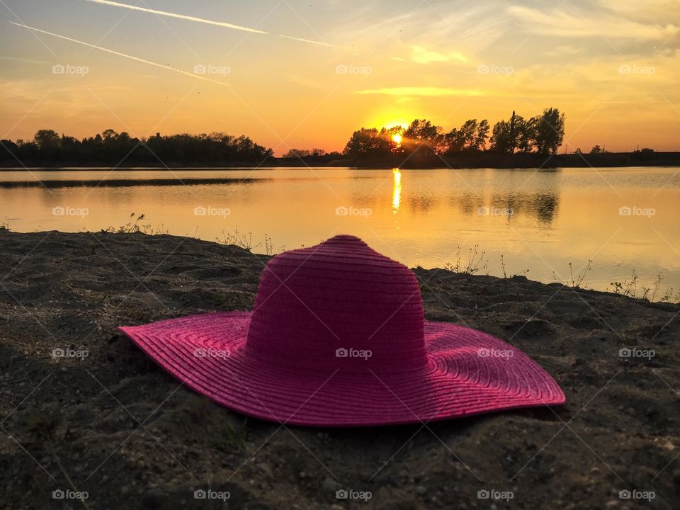 Pink summer hat on the sand near the lake during golden hour