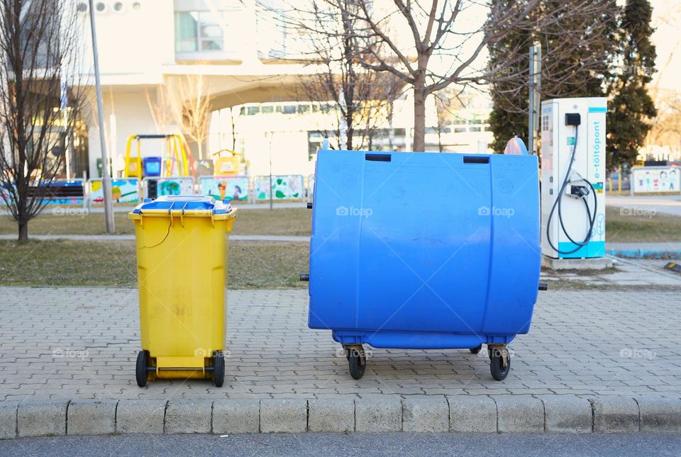 two garbage cans, yellow and blue, stand in the center of the city