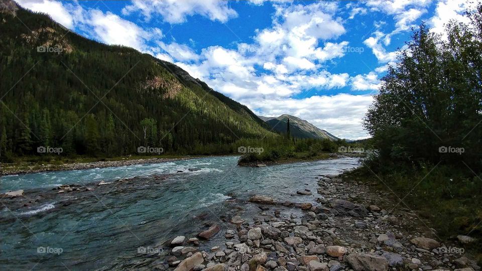 Aquamarine river waters flow through majestic mountains of British Columbia, Canada on a blue sky day.