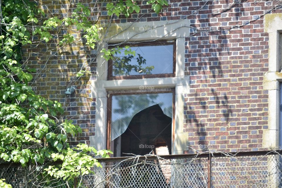 A shattered window on a brick wall with twisted metal below and leaves surrounding 