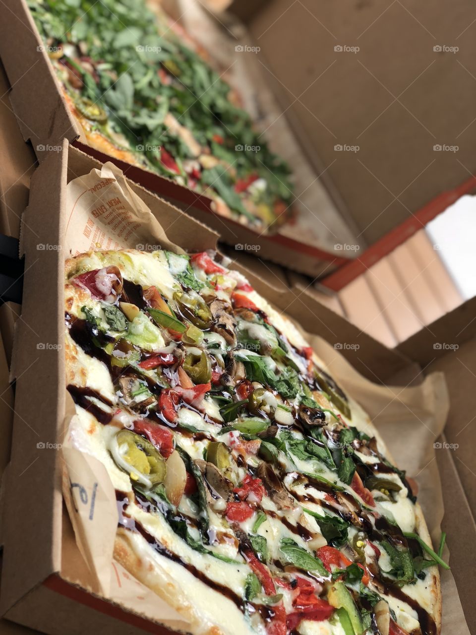Two pizzas in boxes with one in focus 