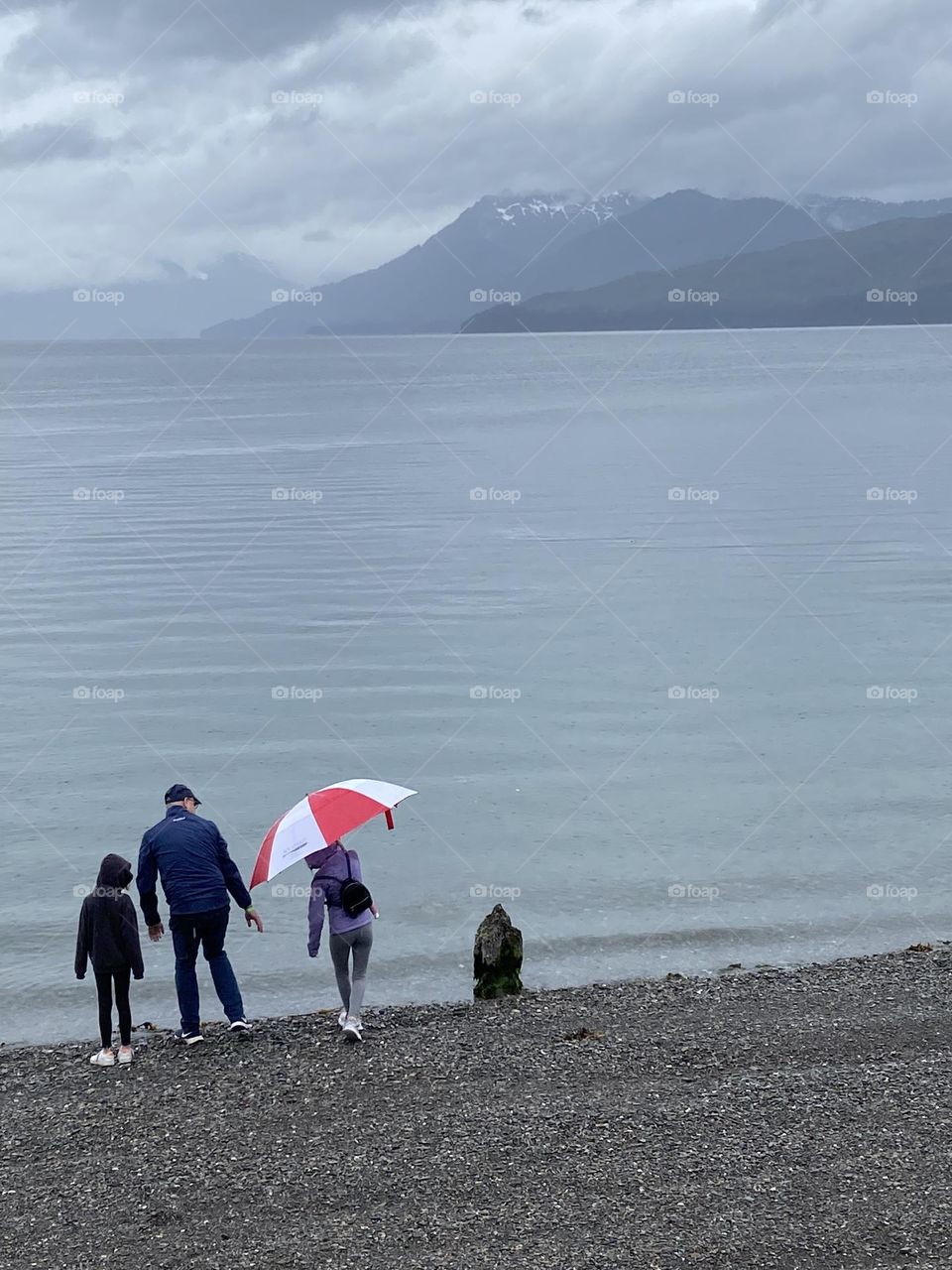 Family by the sea with bright red umbrella.