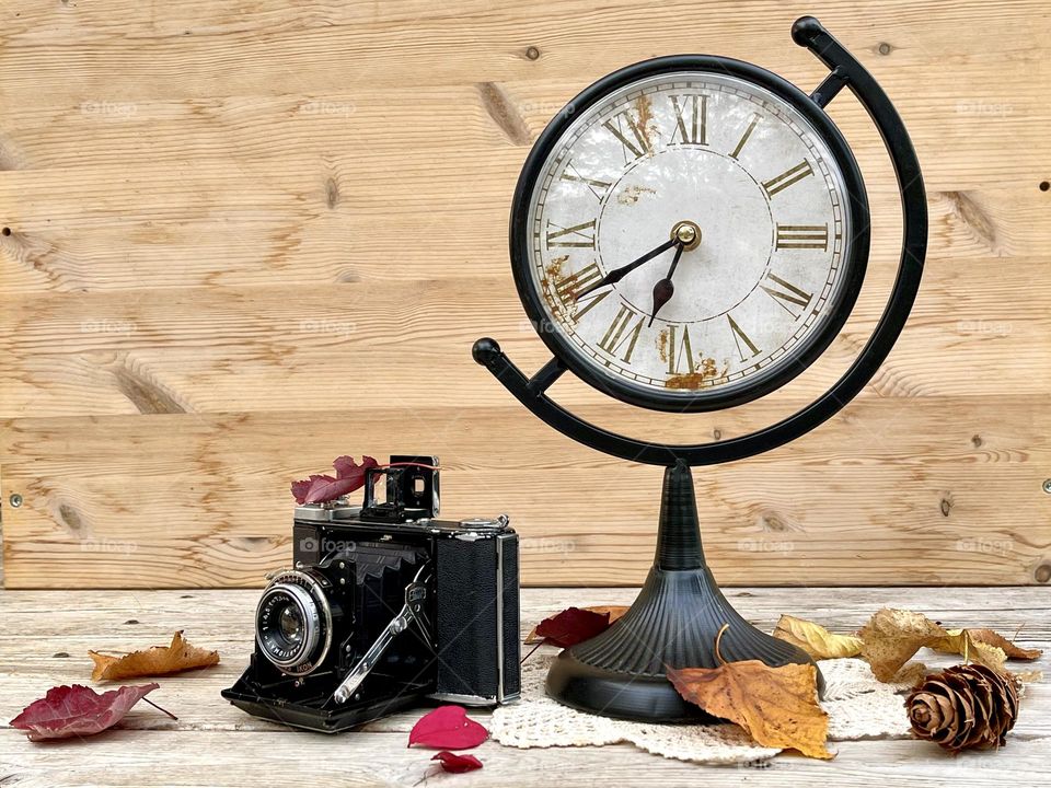 Retro autumn composition with clock, retro camera, orange leaves 