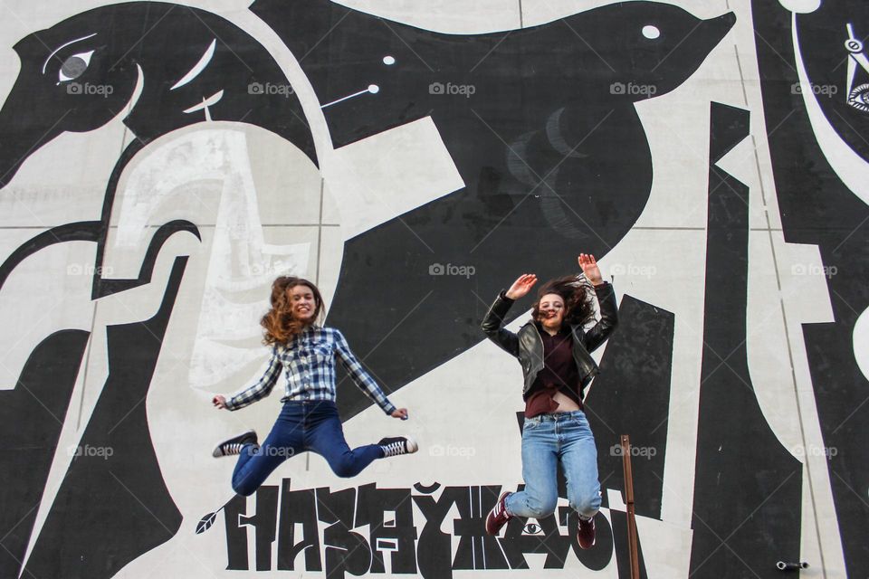 Two girls jumping near a graffiti wall. On the inscription is the word Forever