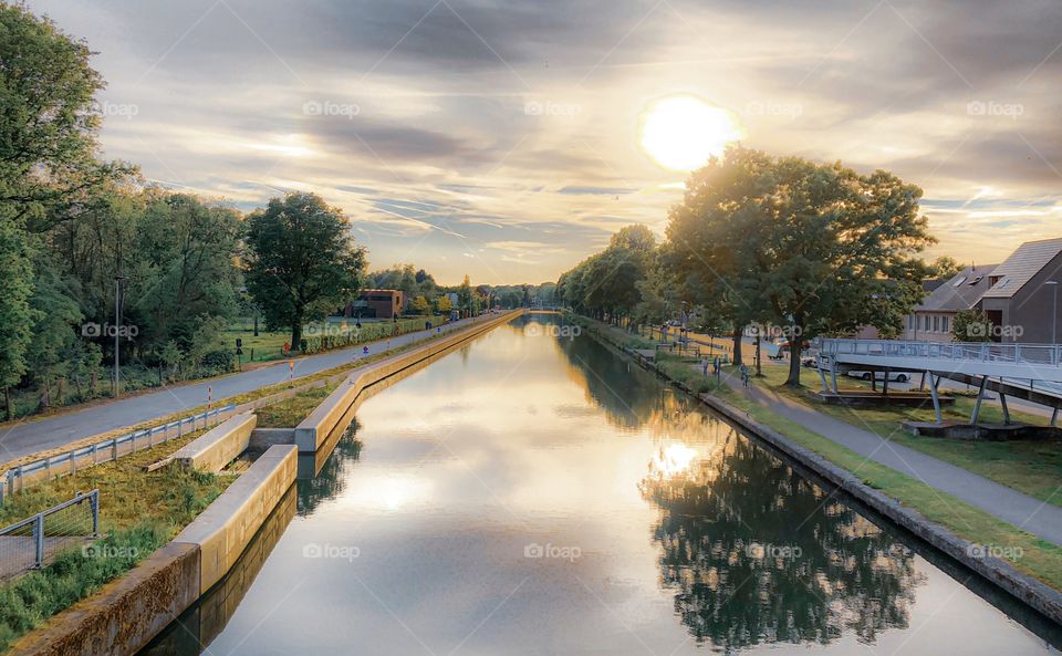 Sunset in a soft Clouded sky reflected in the water of a canal or river surrounded by trees