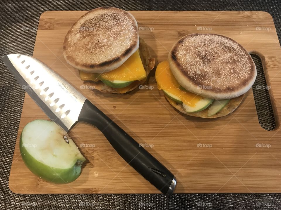 A delicious English muffin with melted cheese and sliced apples inside displayed on a cutting board in the kitchen. USA, America