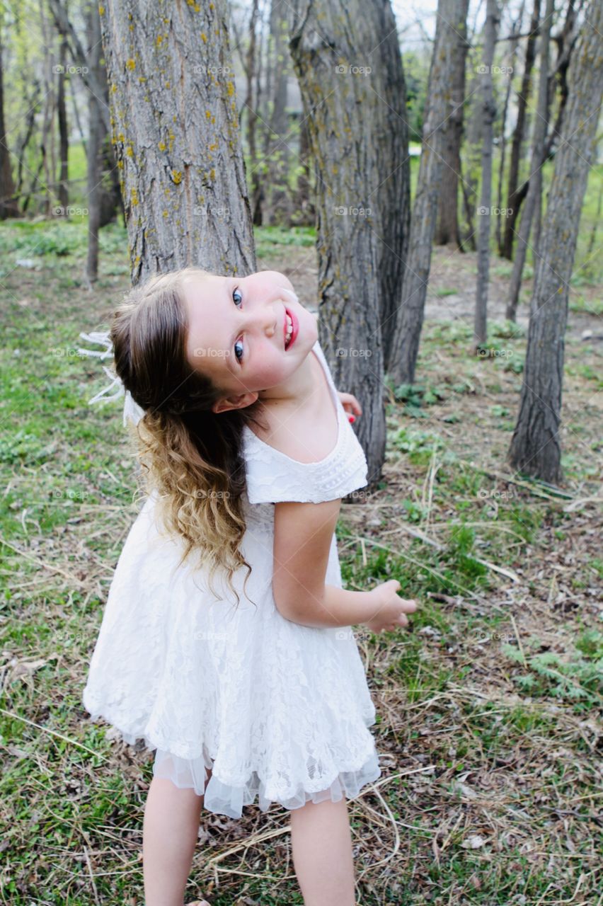 Darling little girl in beautiful white dress and white bow posing in front of trees! 