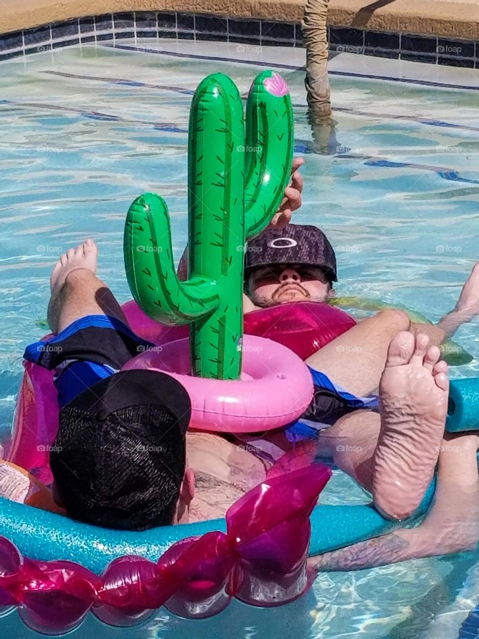 A couple of guys relaxing and escaping the summer heat by floating in the pool with flotation devices in the cool water 