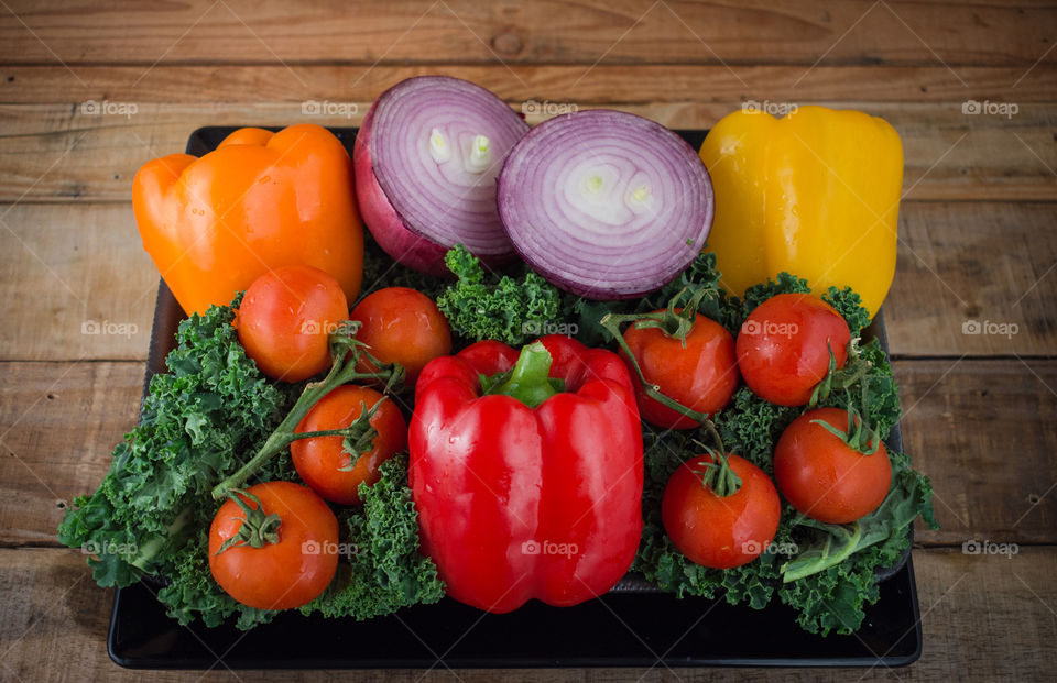 colorful plate of fresh vegetables including red, yellow, and orange peppers, cherry tomatoes, red onion, and kale on a wood table