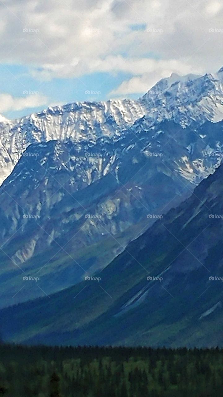 Very much like an oil painting. the emerald slopes of Alaska's rugged snowed covered majestic mountains flow down to the forests below .