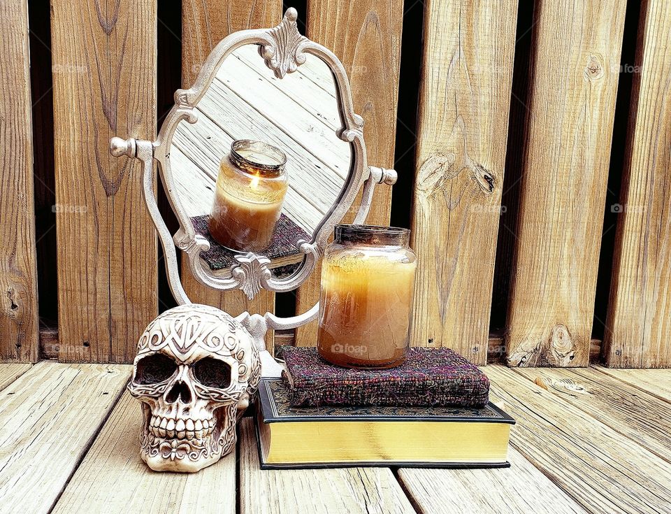 skull and candle sitting on a pile of books in frount of a mirror