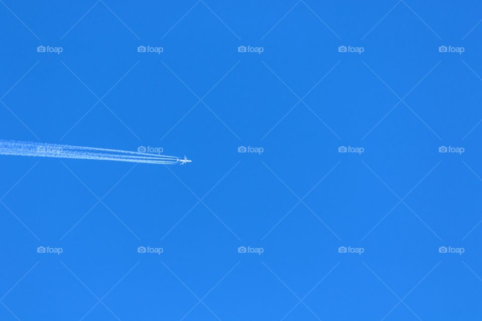 airplane flies high in the intense blue sky, leaving behind a large trail. Perfect Sky in a sunny day