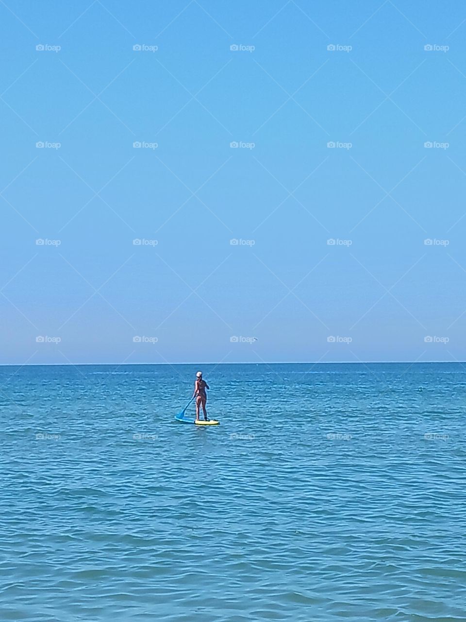 Peacefully paddling towards the horizon on a calm sea.