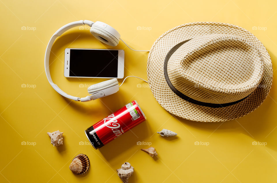 Travel under Covid-19 and new normal concept. Top view of medical face mask, can of Coca-Cola, phone and beach hat on yellow background. Creative ideas of prevent Coronavirus