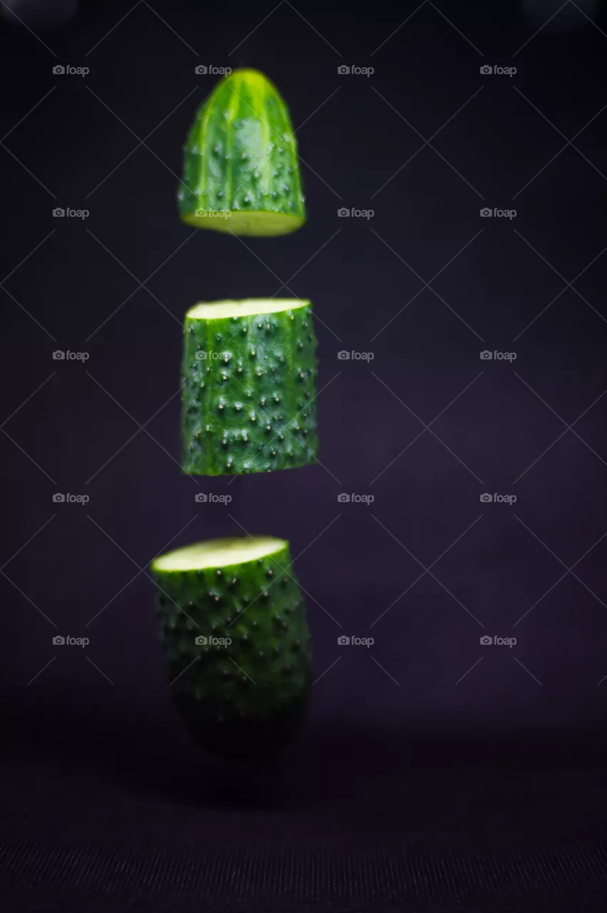 Close-up of a cucumber cut into three parts in the air on a black background.