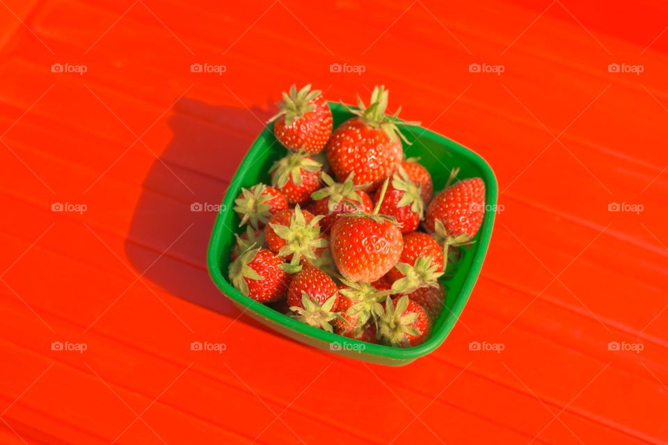 Freshly picked strawberries in a green bowl with red background