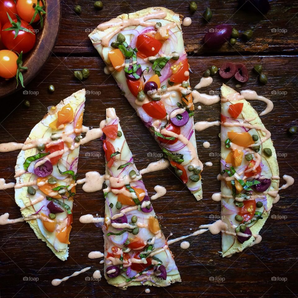 Hummus Pizza on flatbread with cherry tomatoes, olives, capers, fresh basil and red pepper cashew cheese sauce. 
