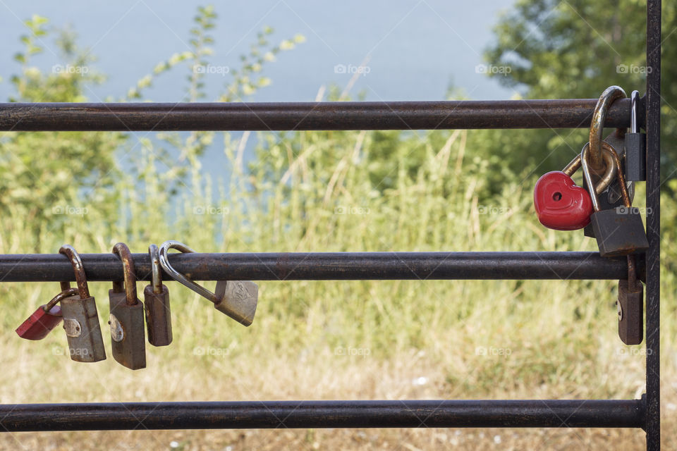 Red padlock with shape of heart and metal padlocks on the fence