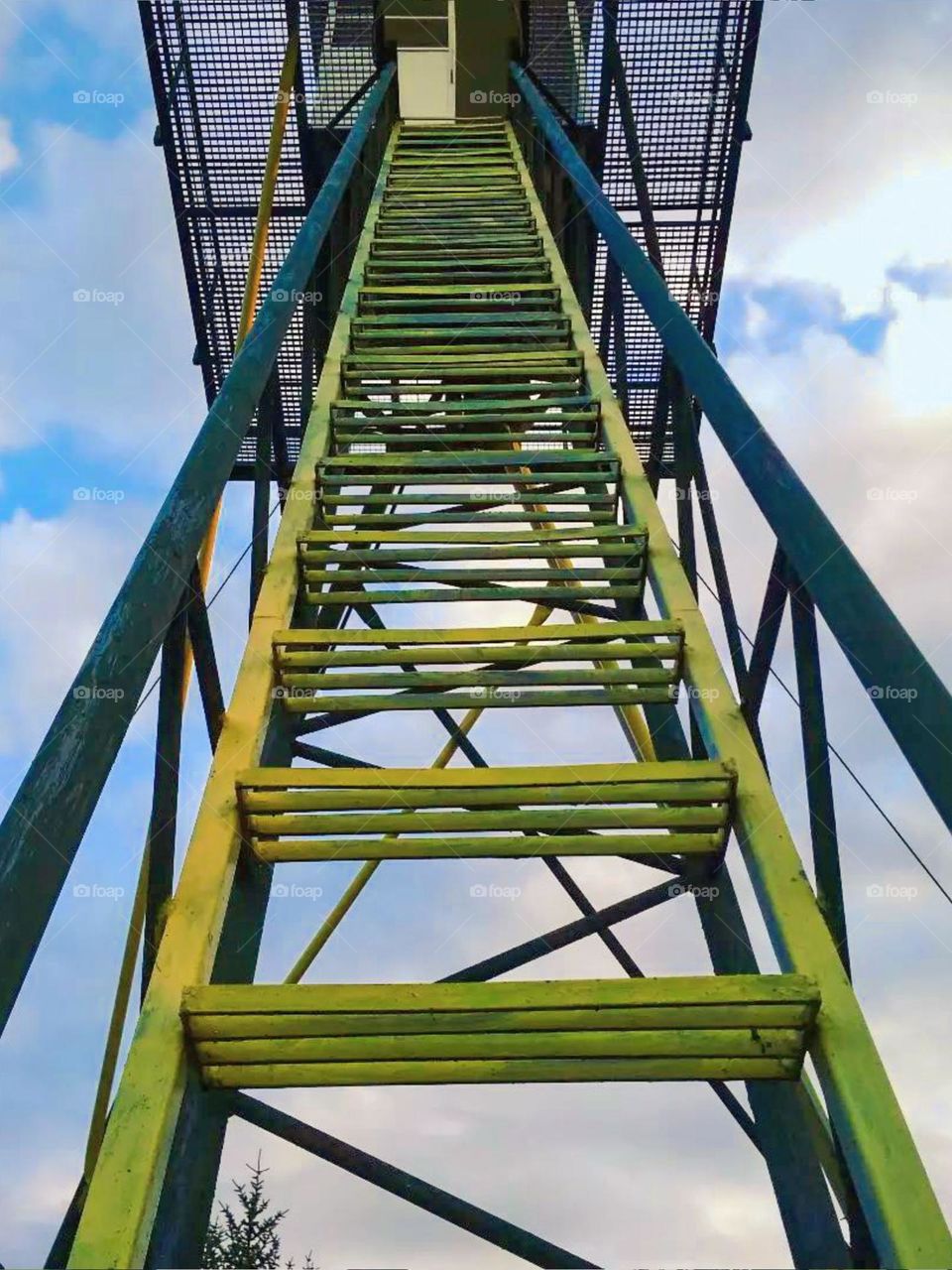 Close-up view of wooden stairs leading upwards, with cloudy sky in the background. These stairs appear to lead to a platform or higher structure, perhaps a watchtower or observation platform