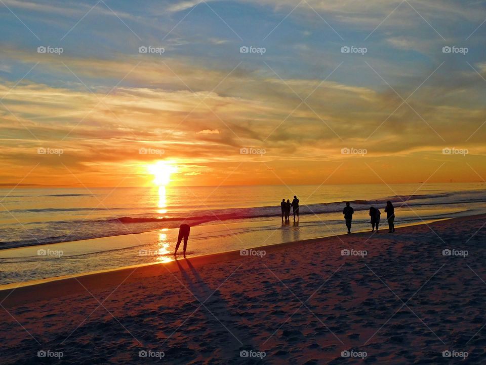 People on the beach at sunset. The big orange and yellow ball slowly going down and down as it sets into the horizon making the sky absolutely stunning