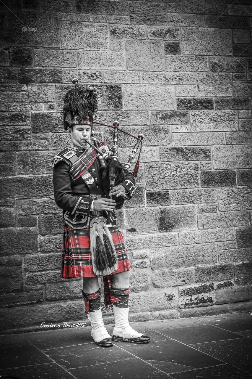 Bagpiper playing music with bagpipe in front of wall