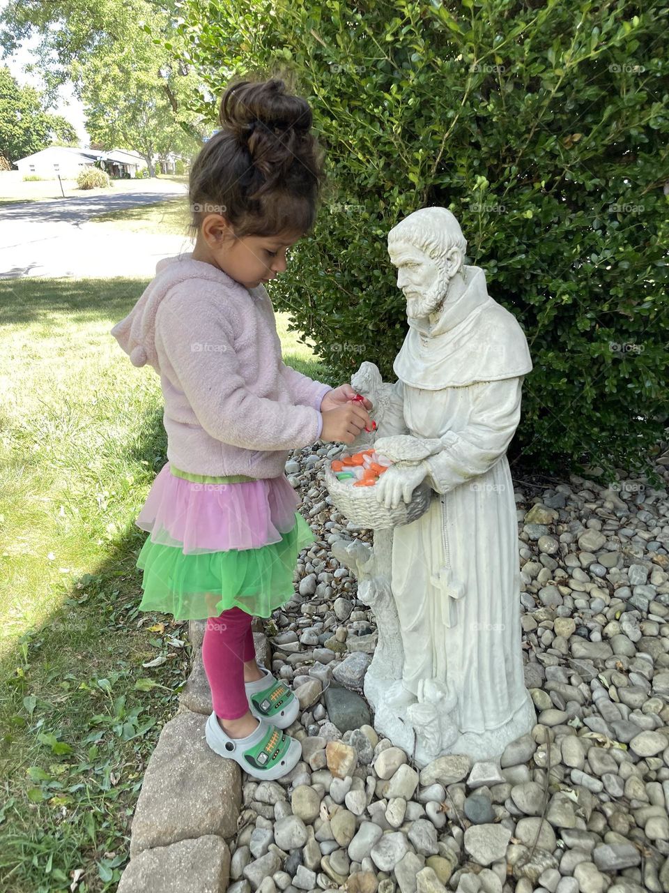 Little girl gives colorful rocks to statue, little girl loves Saint Francis of Assisi, putting colorful rocks into basket of a statue