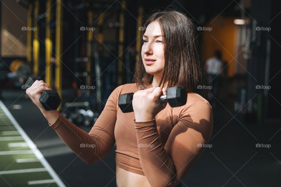 Young brunette woman training her muscles in the fitness club gym