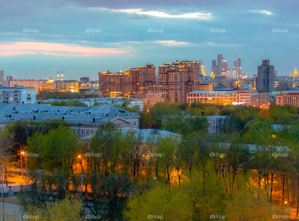 Russia, Moscow, Lefortovo. View of the spring evening city with blossoming trees, the setting sun and lights. City spring evening landscape with modern and historical architecture