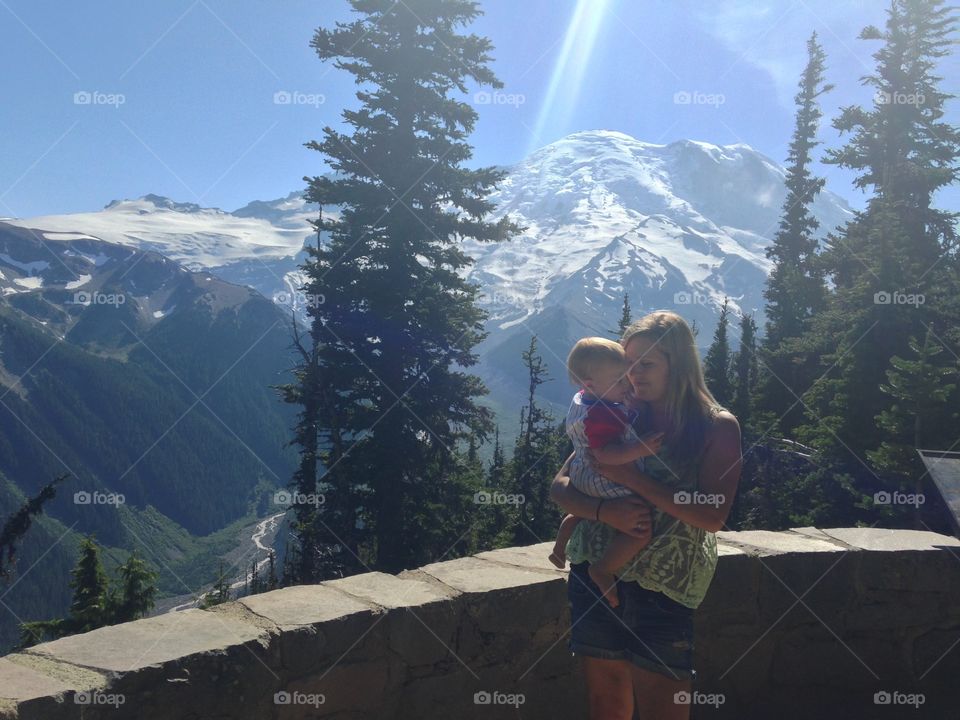 Woman holding kid against mountain in winter