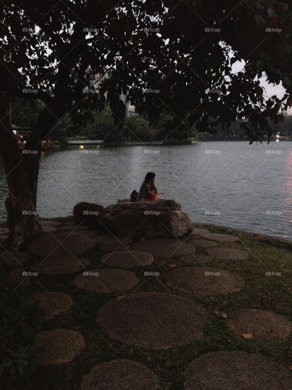 Sitting alone on a stone under a tree at the lake bank