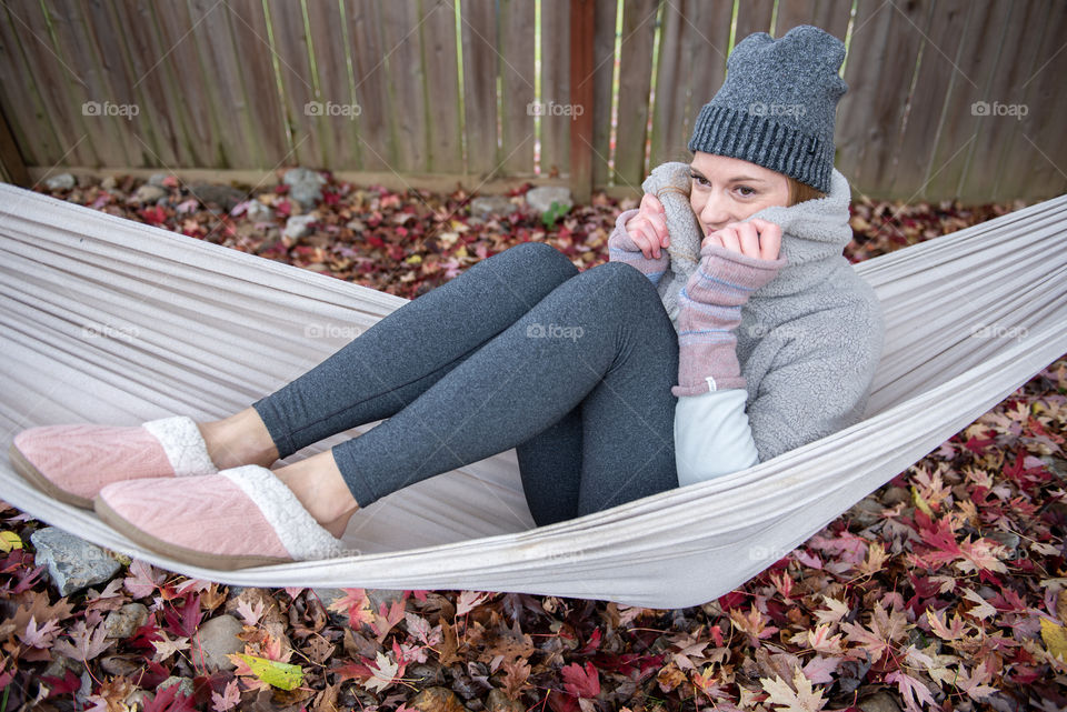 Close-up of a young millennial woman sitting in a hammock and covering her face
