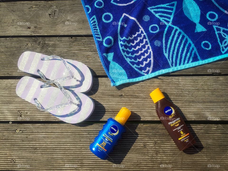 Flat lay summer items on wooden deck: flip flops, towel and Nivea sunscreen