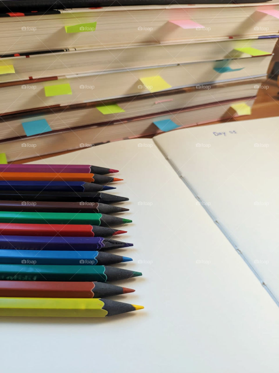 A notebook written day one, several colored pencils and books with post it to mark importante pages to study 