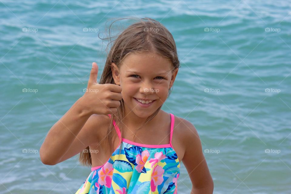 Beautiful happy caucasian child of 7-8 years with thumb up on sea background