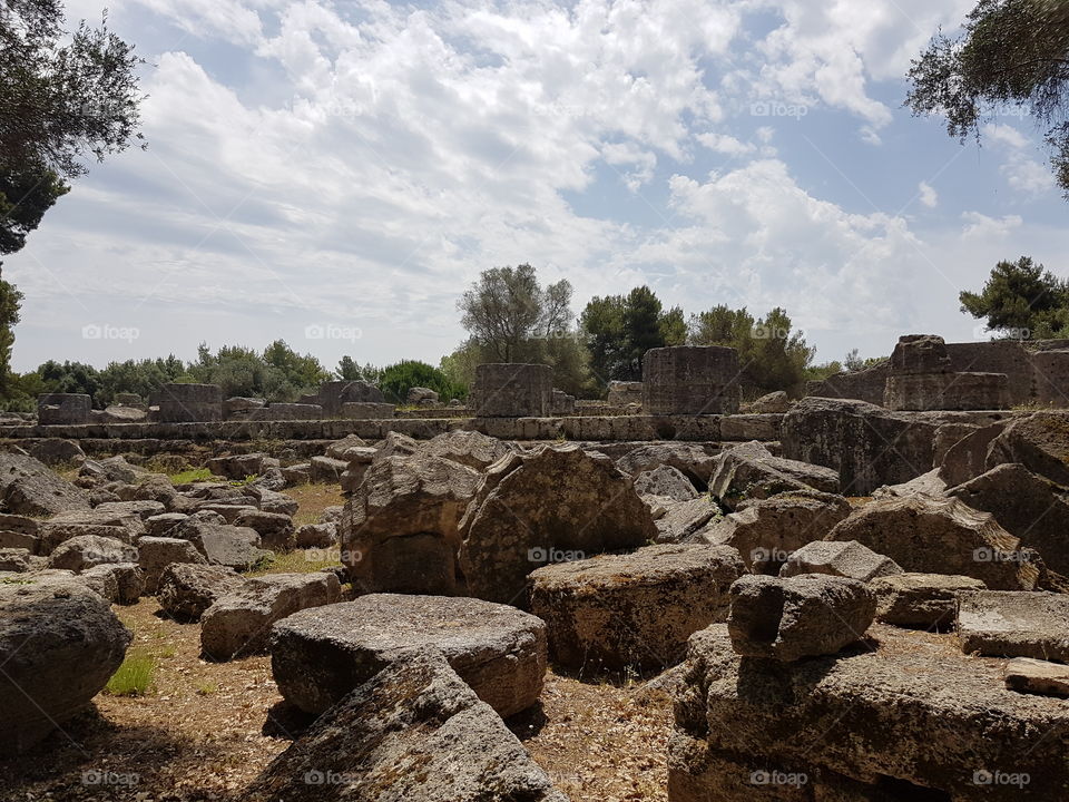 Fallen marble pillars of ancient Greece in Olympia, ruins of historical site on sunny summer day